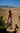 Woman in a long dress standing on a stone wall with mountains in the background